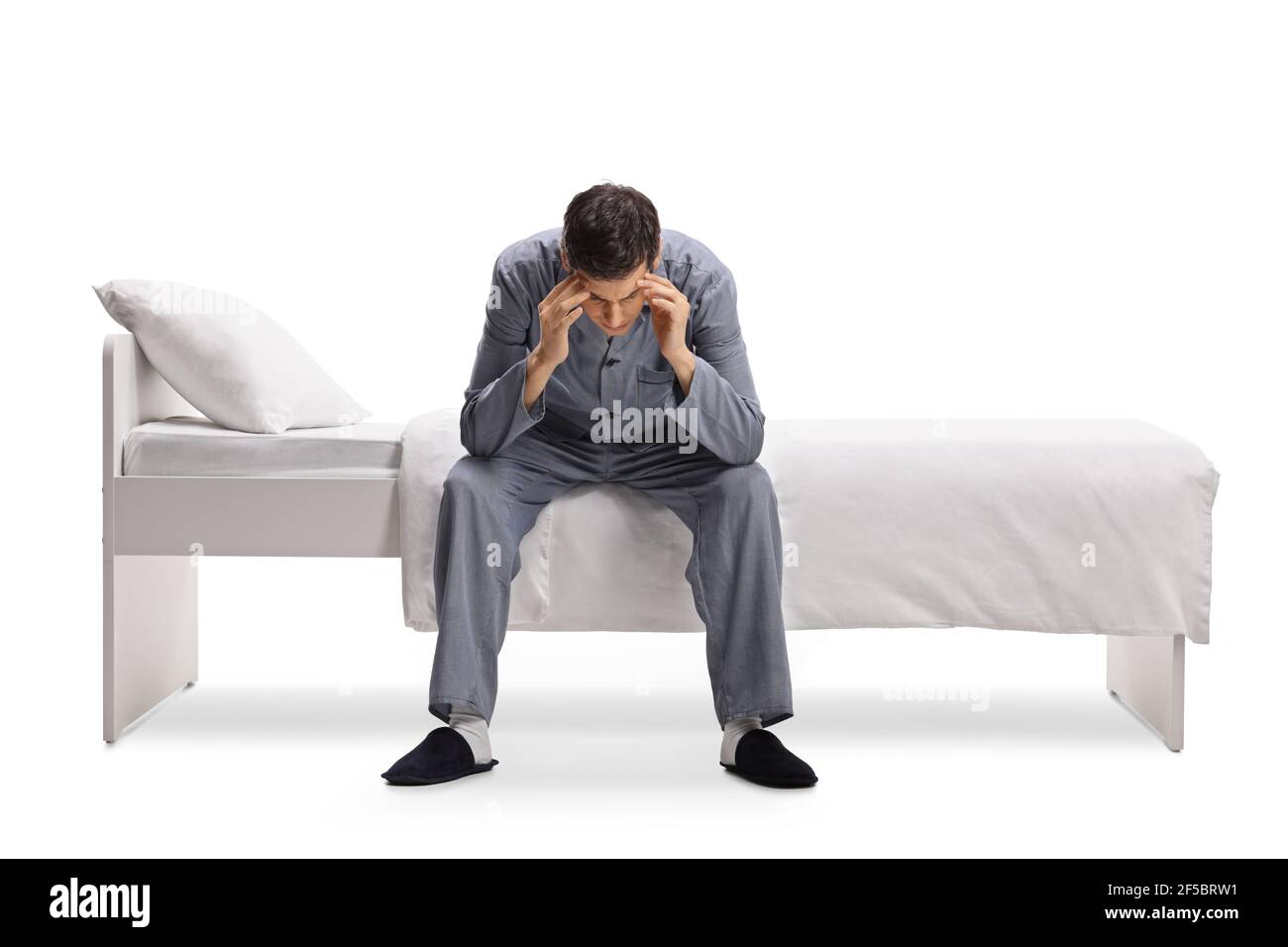 Uomo in pigiama seduto su un letto singolo e tenendo la sua testa si isolò su sfondo bianco Foto Stock