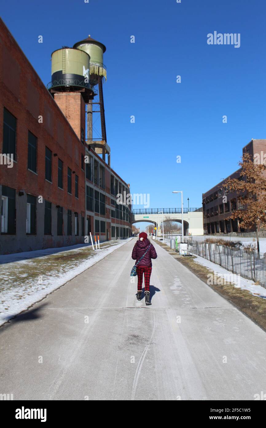 Donna che cammina sul Dequindre Cut Greenway a Detroit in inverno con torri d'acqua d'epoca Foto Stock