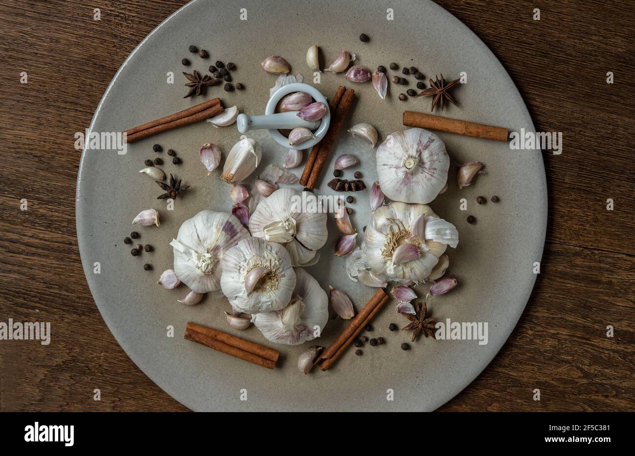 Bulbi d'aglio e spicchi d'aglio con spezie alle erbe, cannella, anice stellato e grano di pepe in ceramica su tavola rustica di legno. Concetto di spazio di copia di Foto Stock