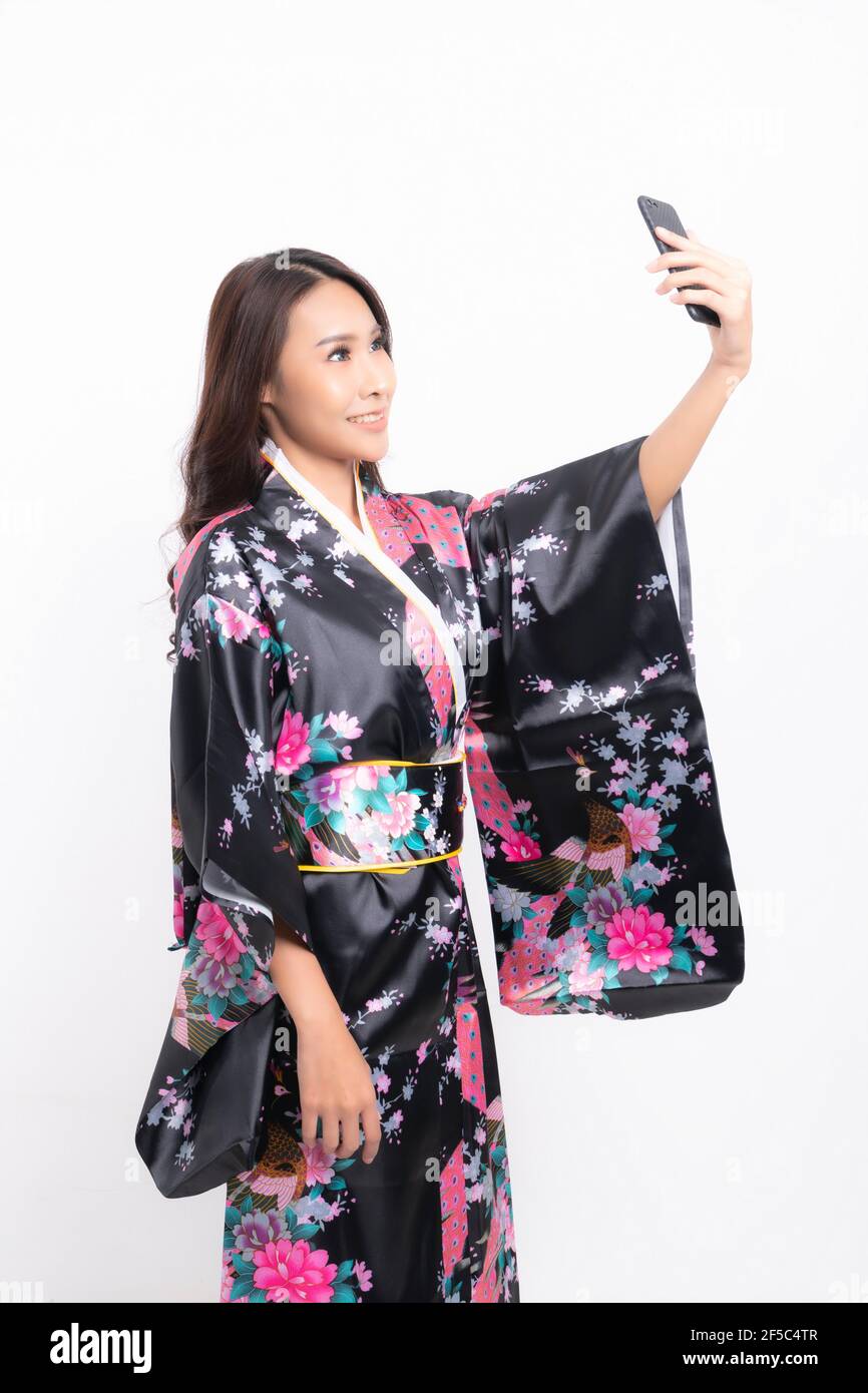 Bella donna asiatica attraente indossando kimono giapponese tradizionale utilizzando un telefono cellulare per prendere un selfie isolato su sfondo bianco Foto Stock