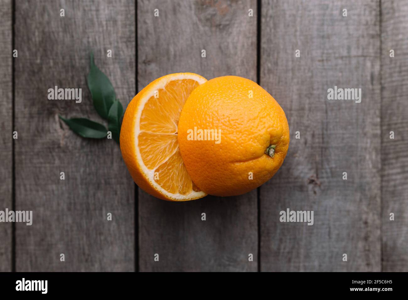 Metà di frutta arancione su sfondo grigio di legno. Polpa di arancia e foglie verdi Foto Stock