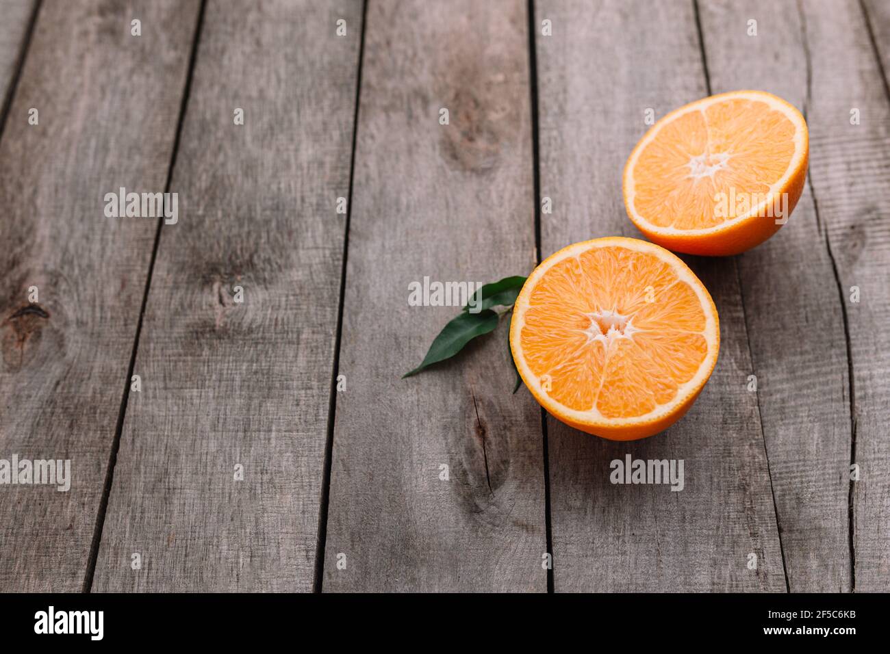 Metà di frutta arancione su sfondo grigio di legno. Polpa di arancia e foglie verdi Foto Stock