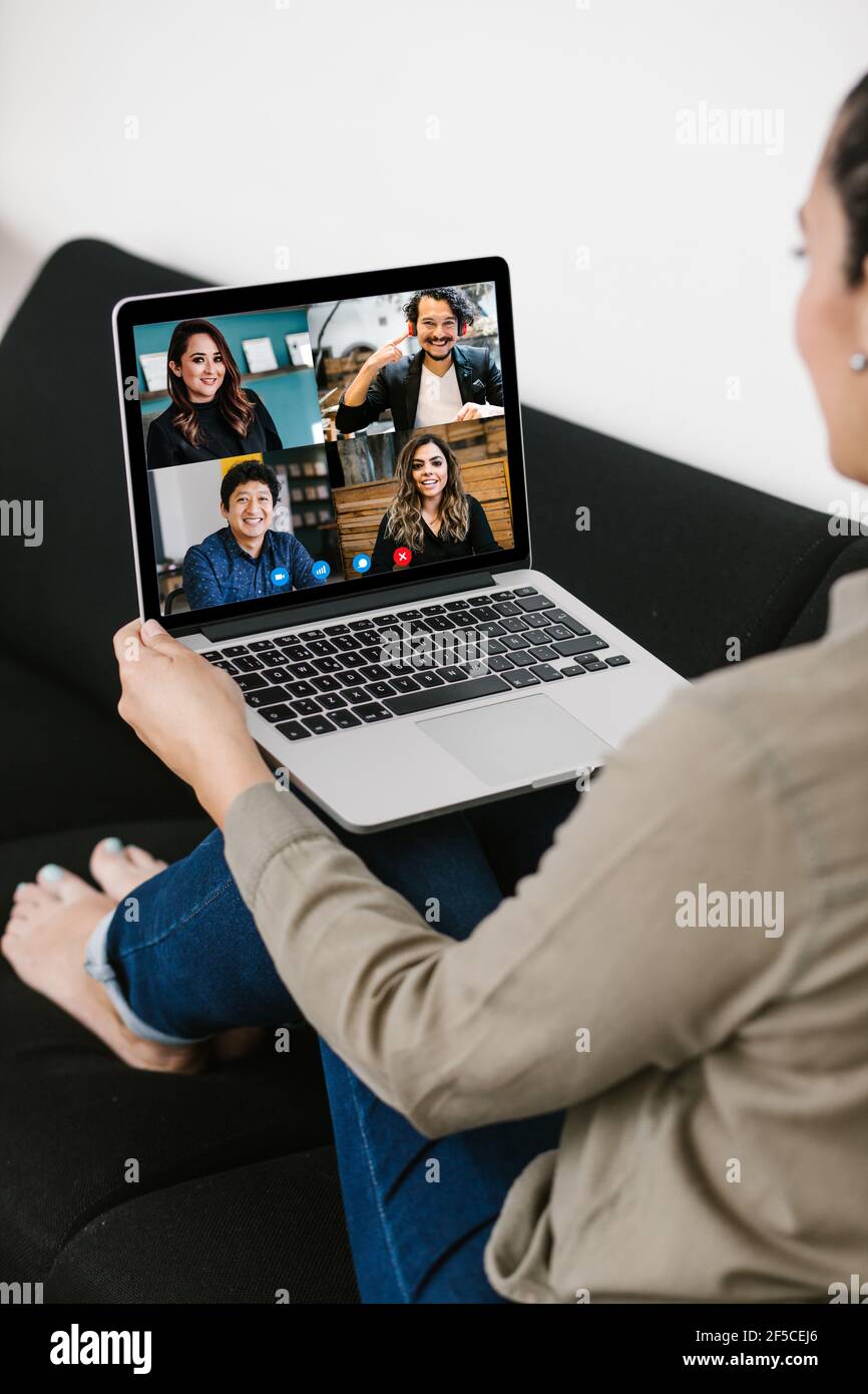 Vista posteriore della donna latina di affari che parla con il suo messicano colleghi del team aziendale di videoconferenza che utilizzano un computer portatile per un riunione online in videochiamata Foto Stock
