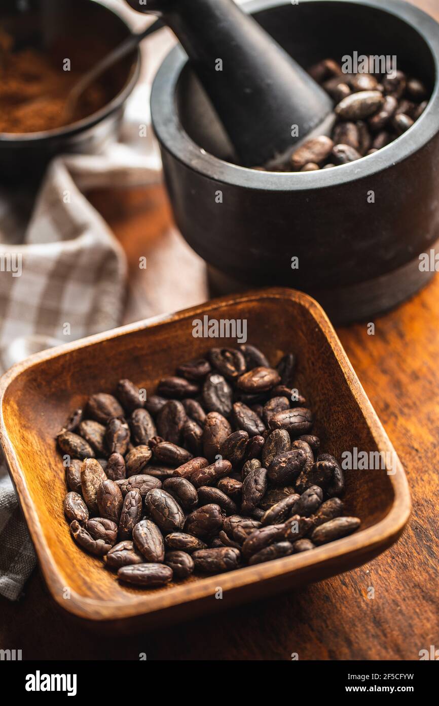 Fagioli di cacao arrostiti in ciotola su tavola di legno. Foto Stock