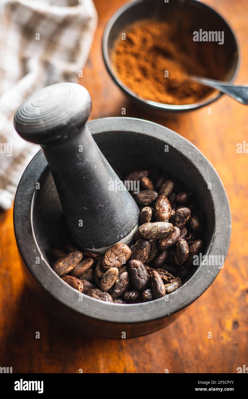 Fagioli di cacao arrostiti in mortaio su tavola di legno. Foto Stock