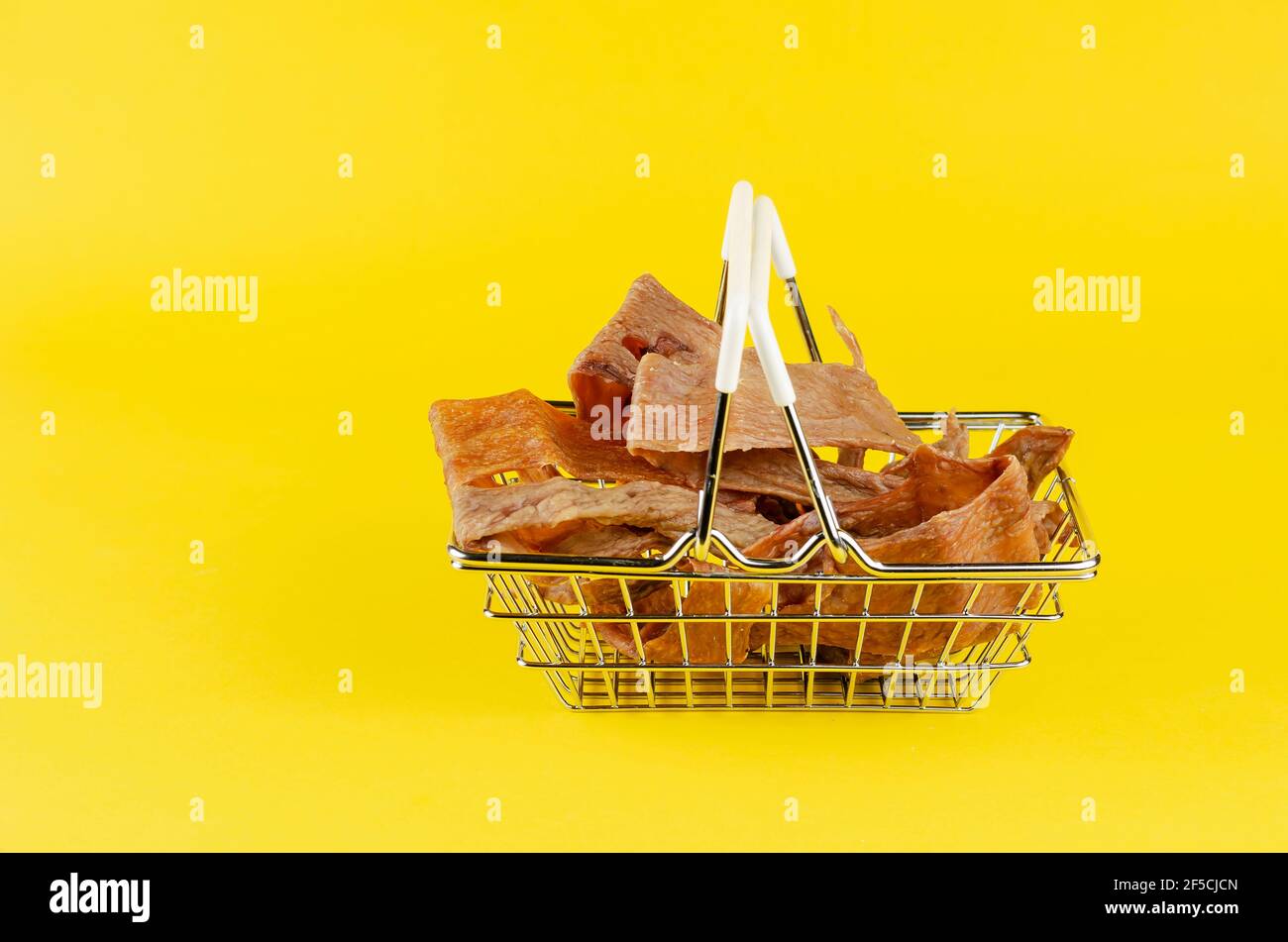 Cestino con le prelibatezze del cane su sfondo giallo. Dolcetti essiccati naturali per animali domestici. Pezzi di mammelle di vacca essiccate. Manzo a scatti per i cani. Supplemento per animali domestici Foto Stock