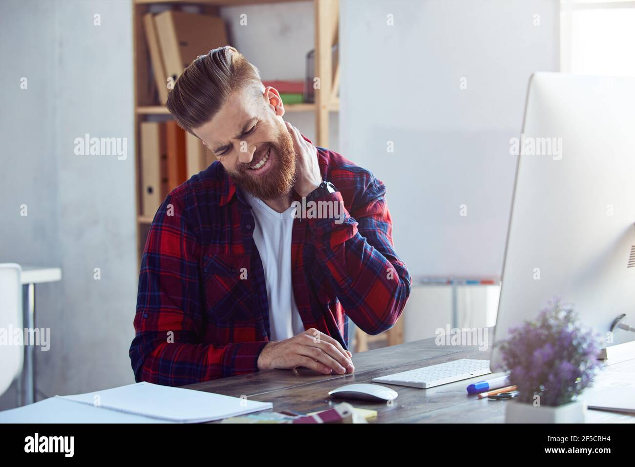 Giovane uomo bearded che ottiene un dolore del collo nell'ufficio Foto Stock