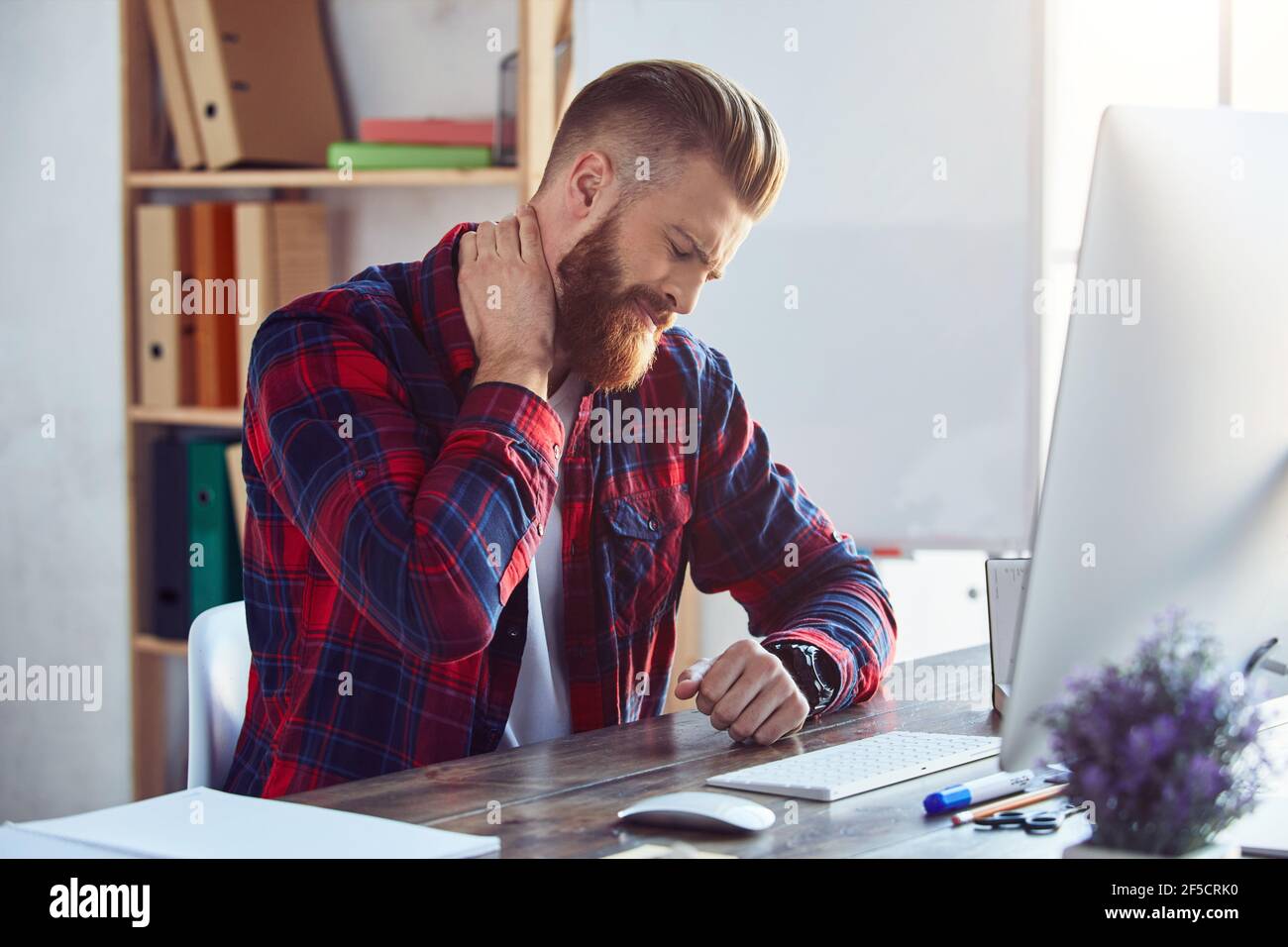 Giovane uomo bearded stanco di lavorare su pc in ufficio Foto Stock
