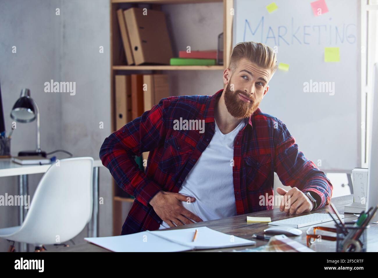Un giovane dipendente di sesso maschile malsano è seduto in ufficio Foto Stock