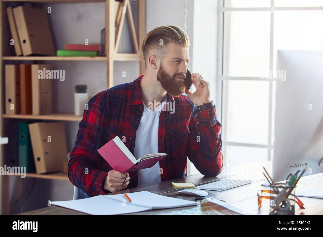 Un giovane sorridente che parla al telefono in ufficio Foto Stock