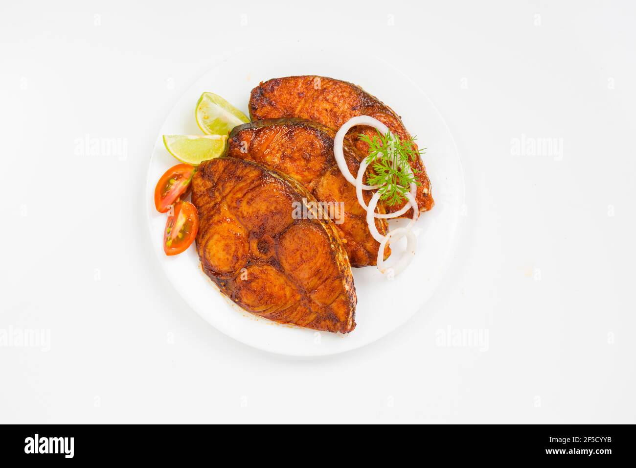 Friggere il pesce ben arrangiato e guarnito con cipolla, limone e pomodoro a fette su un piatto di ceramica bianca con fondo testurizzato bianco. Foto Stock