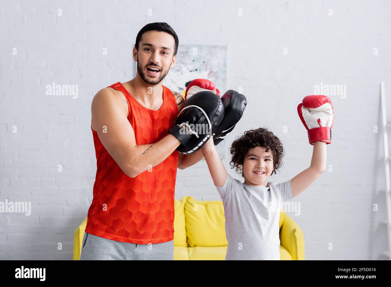 Felice padre musulmano in pugno miti alzando la mano di figlio in guanti da boxe Foto Stock