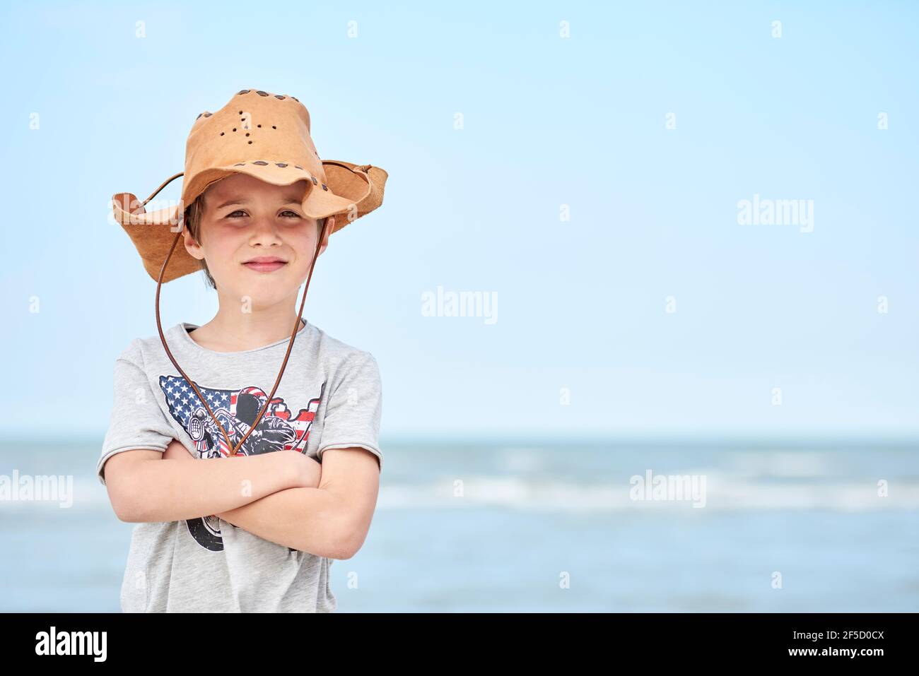 Bambino felice con cappello di cuoio del cowboy che si lascia fotografare  con il mare sullo sfondo. Primo piano di un bambino sorridente con cappello  da cowboy, al Th Foto stock -