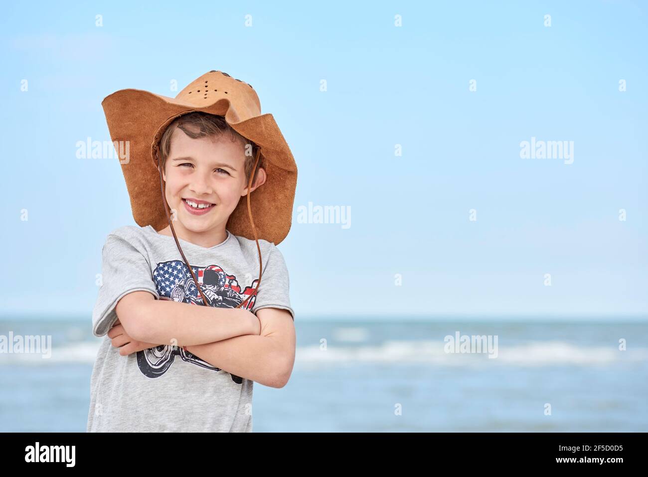 Bambino felice con cappello di cuoio del cowboy che si lascia fotografare  con il mare sullo sfondo. Primo piano di un bambino sorridente con cappello  da cowboy, al Th Foto stock -