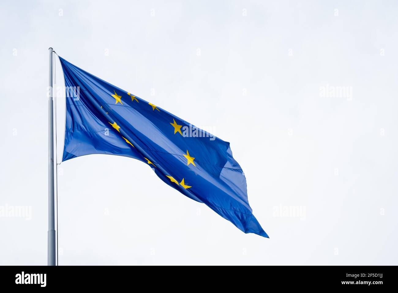 Bandiera dell'Unione europea che sventolava da un flagpole. Sullo sfondo blu, le stelle dorate formano un cerchio come simbolo di unità e solidarietà. Foto Stock