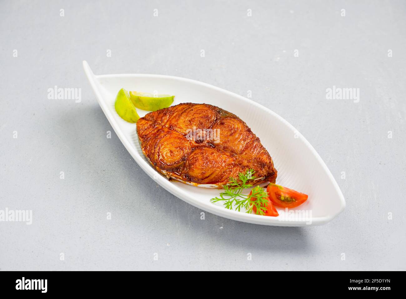 Friggitrice di pesce ben arrangiata e guarnita con cipolla, limone e pomodoro a fette su piastra bianca in ceramica con fondo grigio. Foto Stock