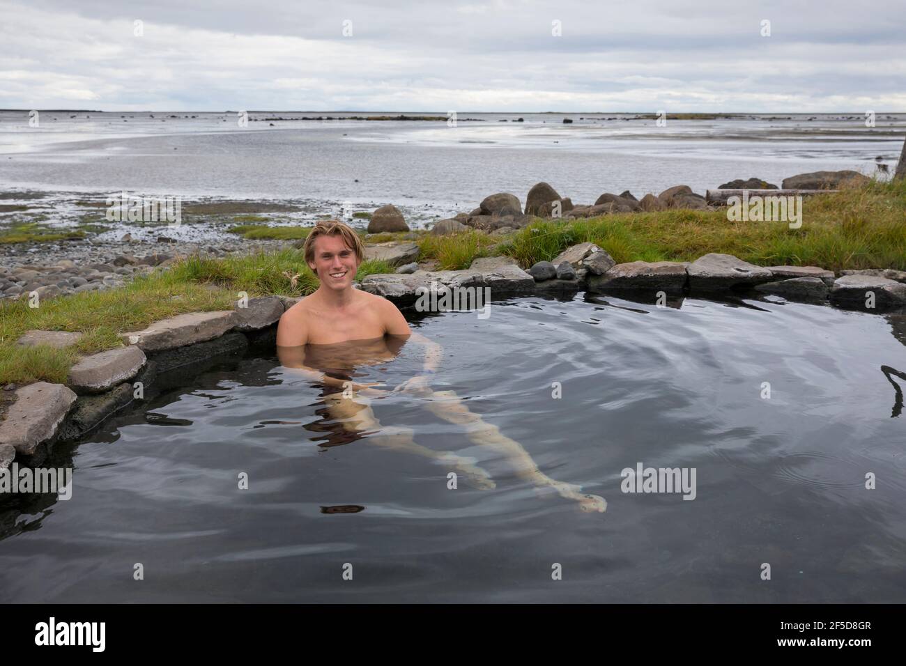 Uomo che bagna nella piscina geotermica naturale di Krosslaug direttamente sulla costa, Islanda, Birkimelur Foto Stock