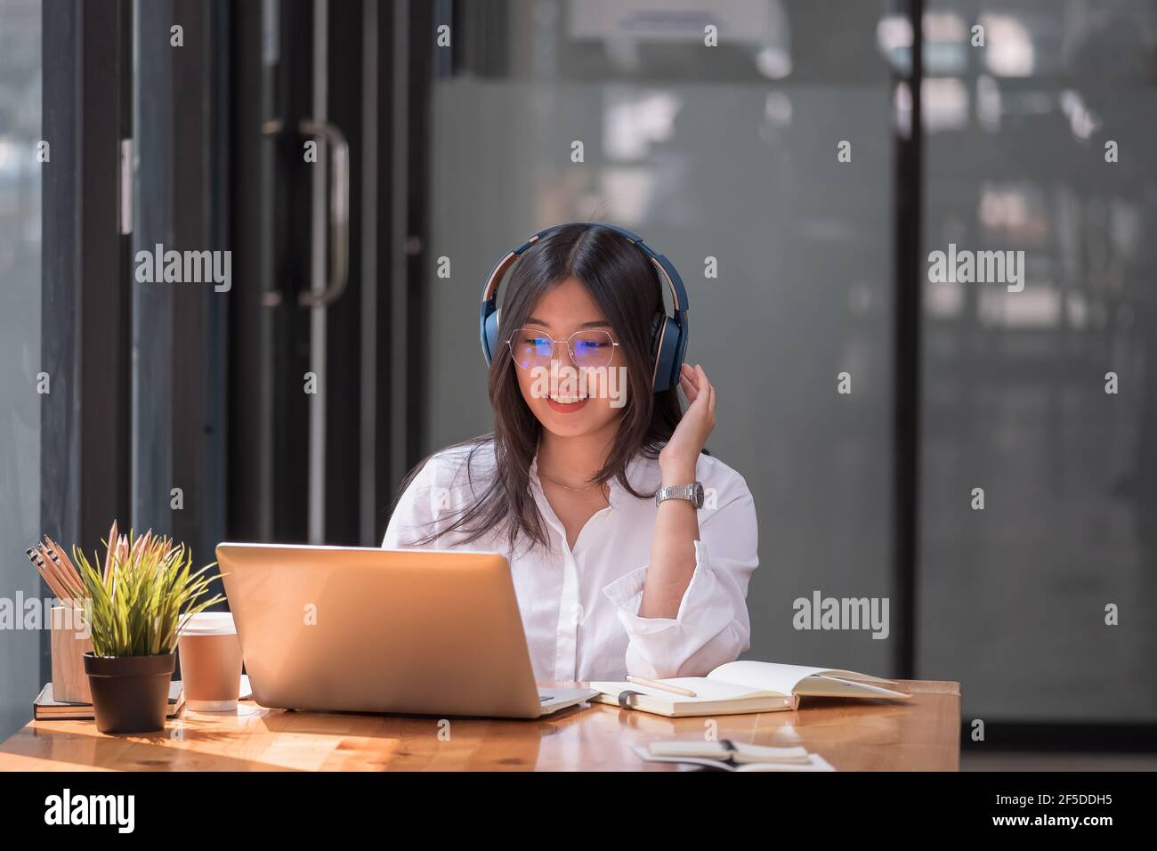 Ragazza asiatica con gli occhiali guardare il computer portatile mentre facendo compiti fare videochiamata all'estero utilizzando la connessione di amici su Internet, formazione online Foto Stock