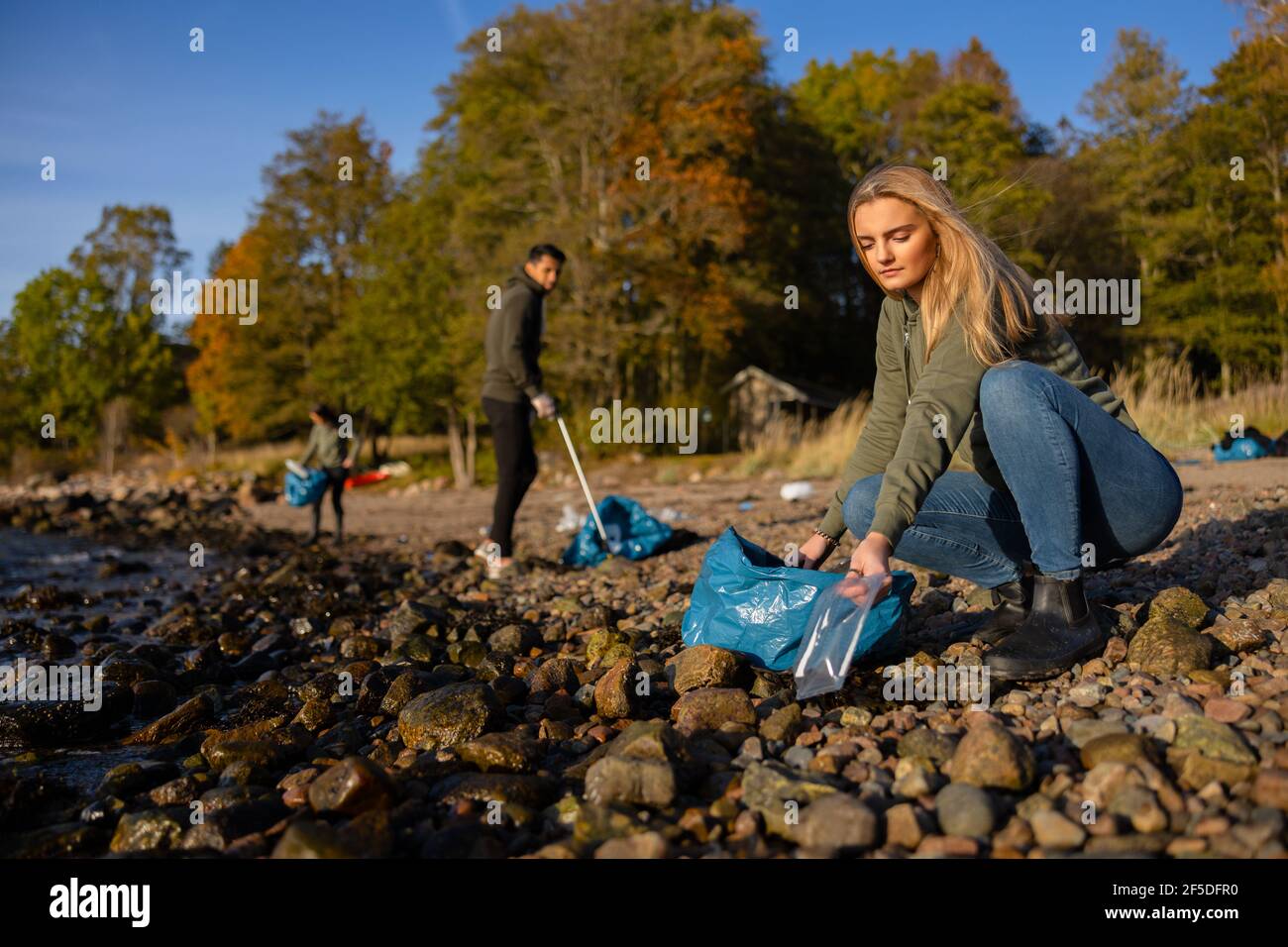 Giovane donna focalizzata nel team di conservazione dell'ambiente che raccoglie la plastica in spiaggia Foto Stock