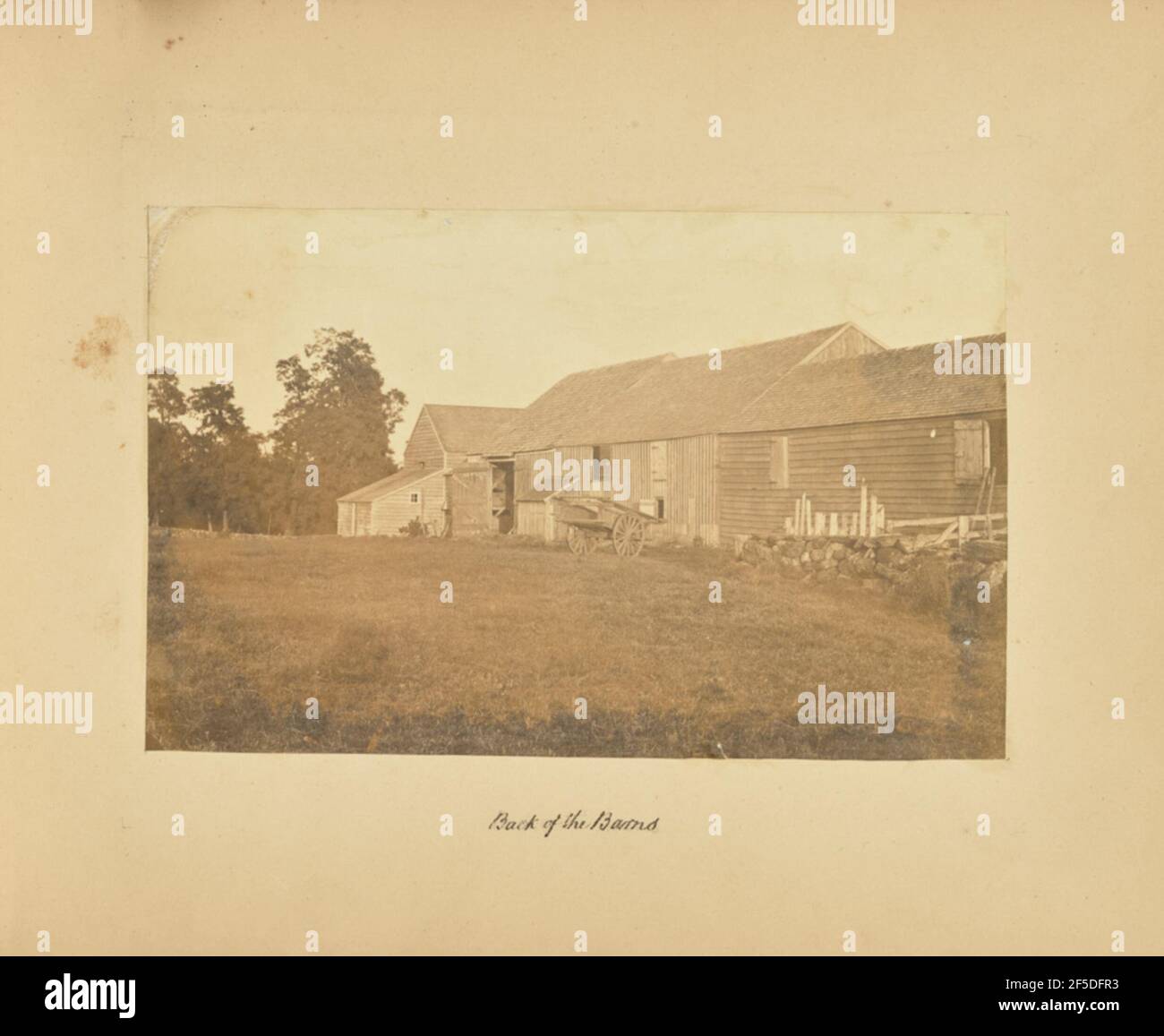 Retro dei granai. Vista sul lato posteriore di una fila di edifici fienile da un prato all'altro. Un grande carrello di legno poggia immediatamente davanti agli edifici, e una parte di un muro di pietra è visibile sul lato destro dell'immagine. (Recto, mount) parte centrale inferiore, scritta a mano in inchiostro nero: 'Retro dei granai' Foto Stock