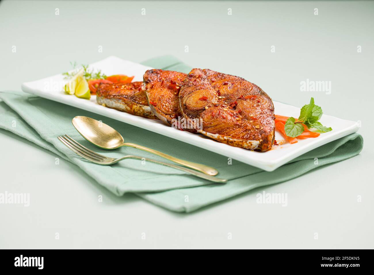 Friggitrice di pesce ben arrangiata e guarnita con fette di cipolla, limone e pomodoro su piatto bianco rettangolare in ceramica di colore azzurro ghiaccio Foto Stock