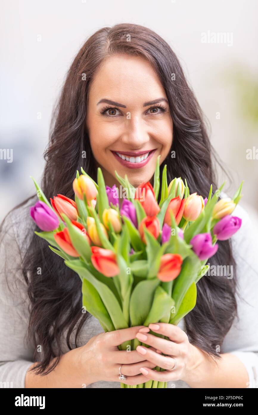 Felice donna dai capelli scuri che tiene in mano un bel bouquet pieno di tulipani durante il giorno nazionale delle donne. Foto Stock