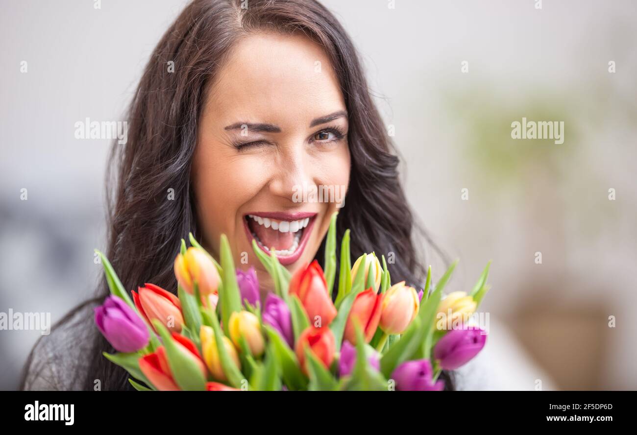 Felice donna dai capelli scuri che lampeggia e tiene un bel bouquet pieno di tulipani durante il giorno nazionale delle donne. Foto Stock