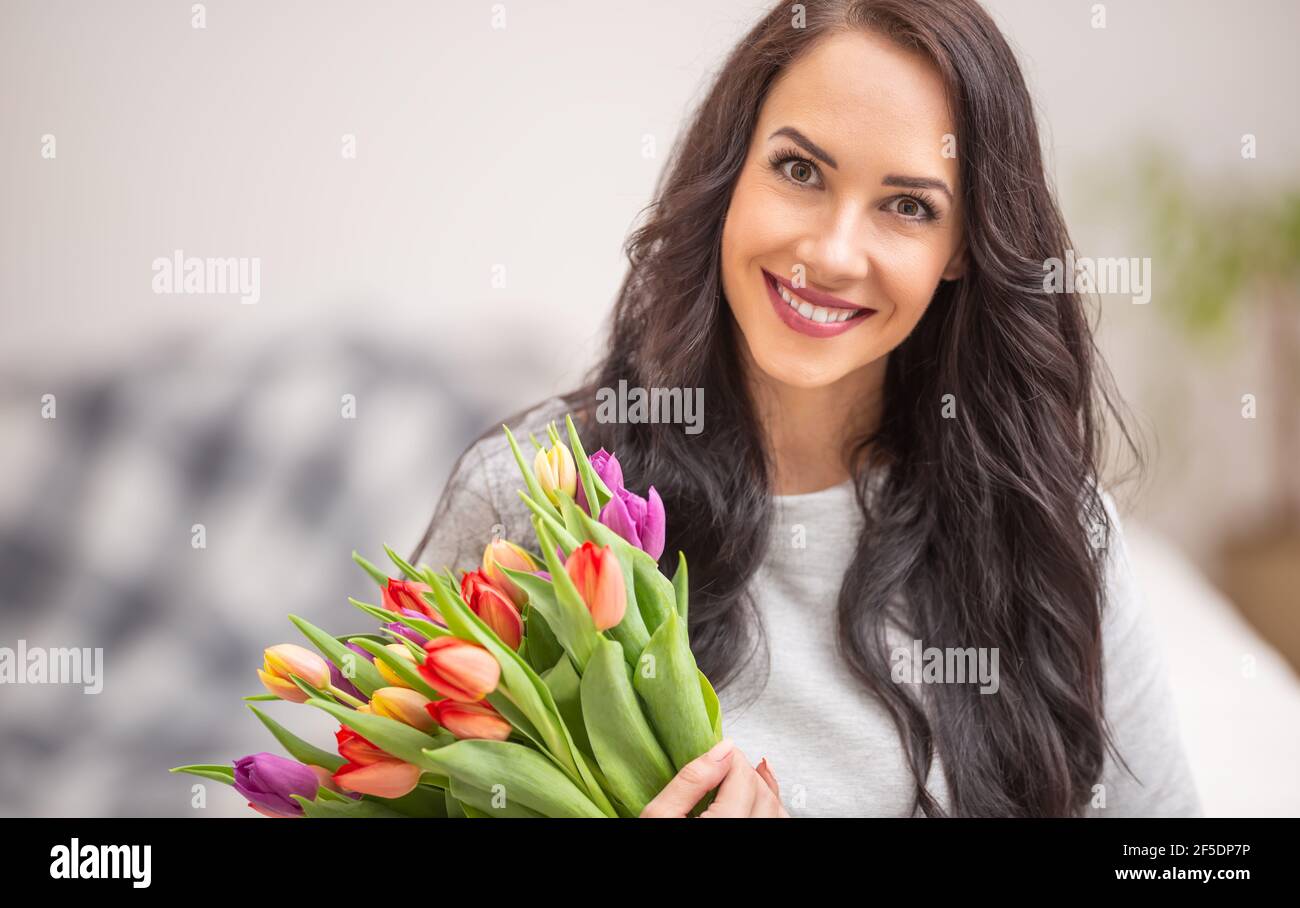 Bella donna dai capelli scuri che tiene in mano un bel bouquet pieno di tulipani durante il giorno nazionale delle donne. Foto Stock