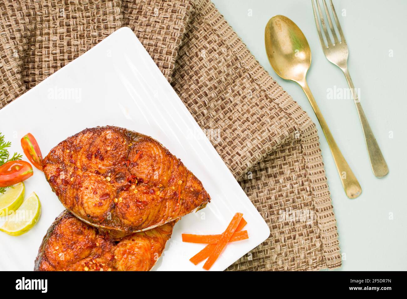 Friggitrice di pesce ben arrangiata e guarnita con fette di cipolla, limone e pomodoro su piastra in ceramica di forma quadrata bianca. Foto Stock