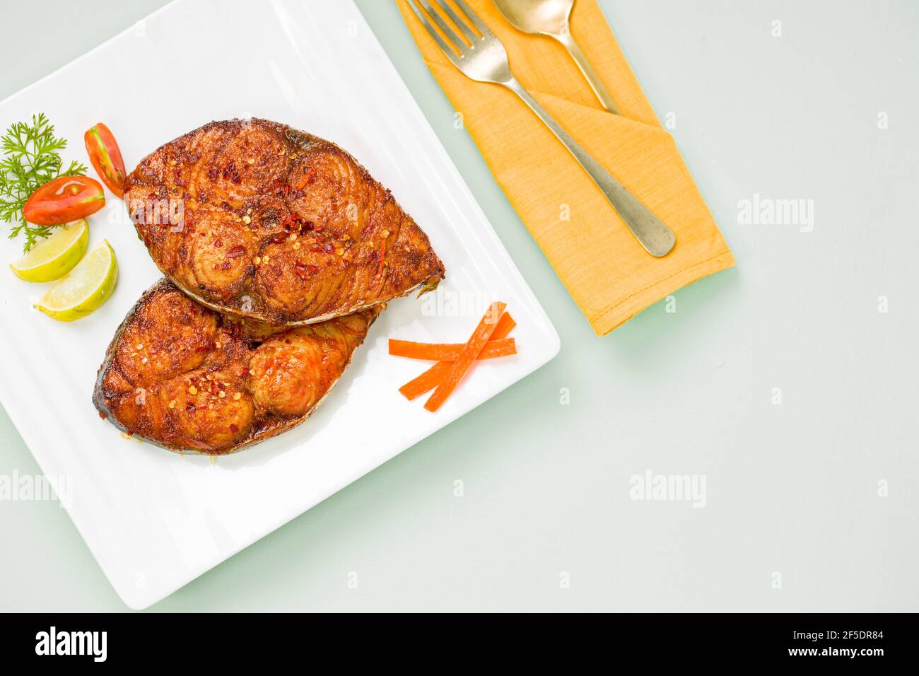 Friggitrice di pesce ben arrangiata e guarnita con fette di cipolla, limone e pomodoro su piastra in ceramica di forma quadrata bianca. Foto Stock