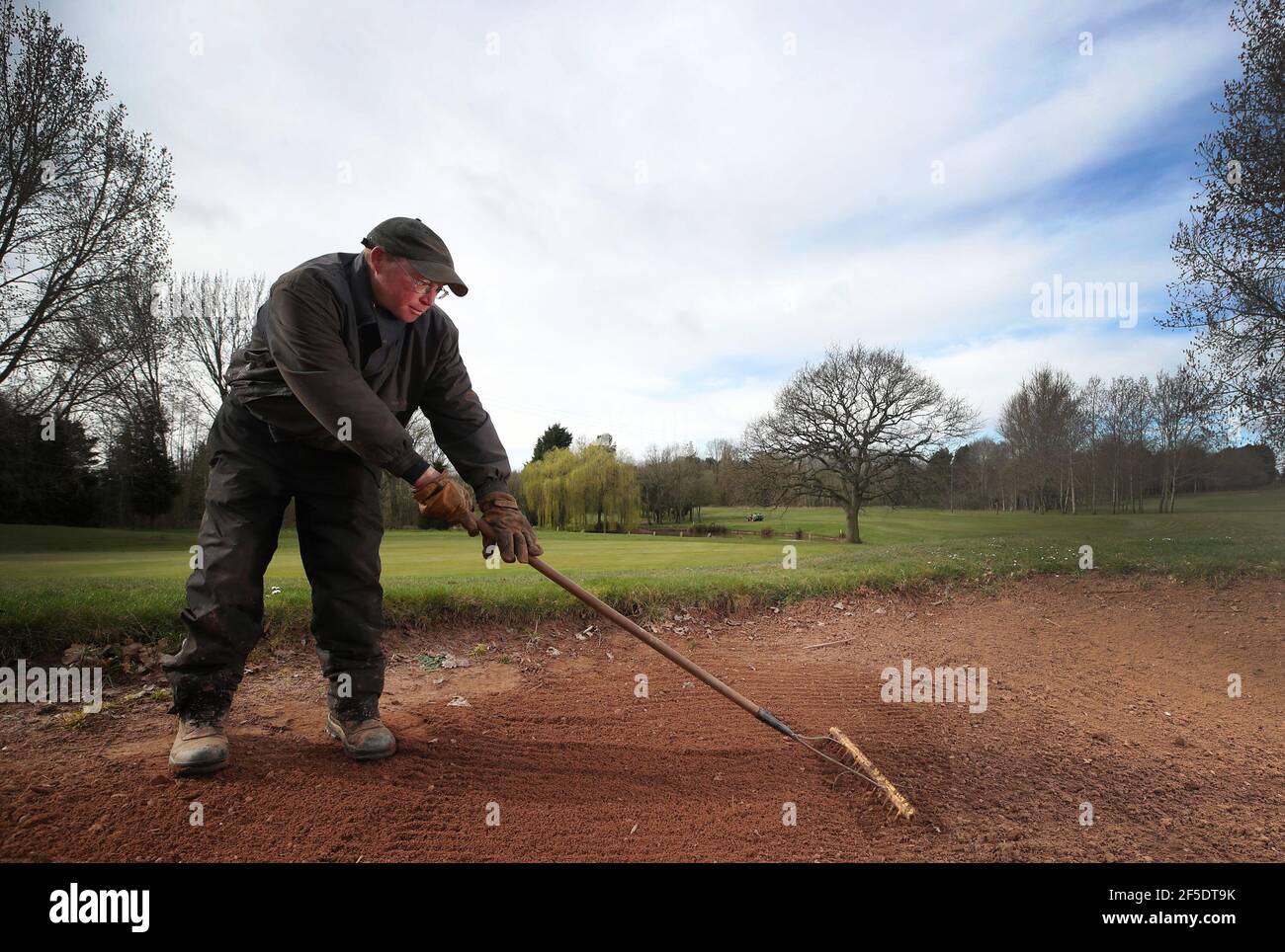 Green Keeper Paul Chantler rastrella un bunker al Telford Hotel and Golf Resort, Shropshire, dove ha lavorato per 34 anni, mentre si preparano per la riapertura dopo che le restrizioni di blocco per gli sport all'aperto e le strutture per il tempo libero sono attenuate. Data di emissione: Venerdì 26 marzo 2021. Foto Stock