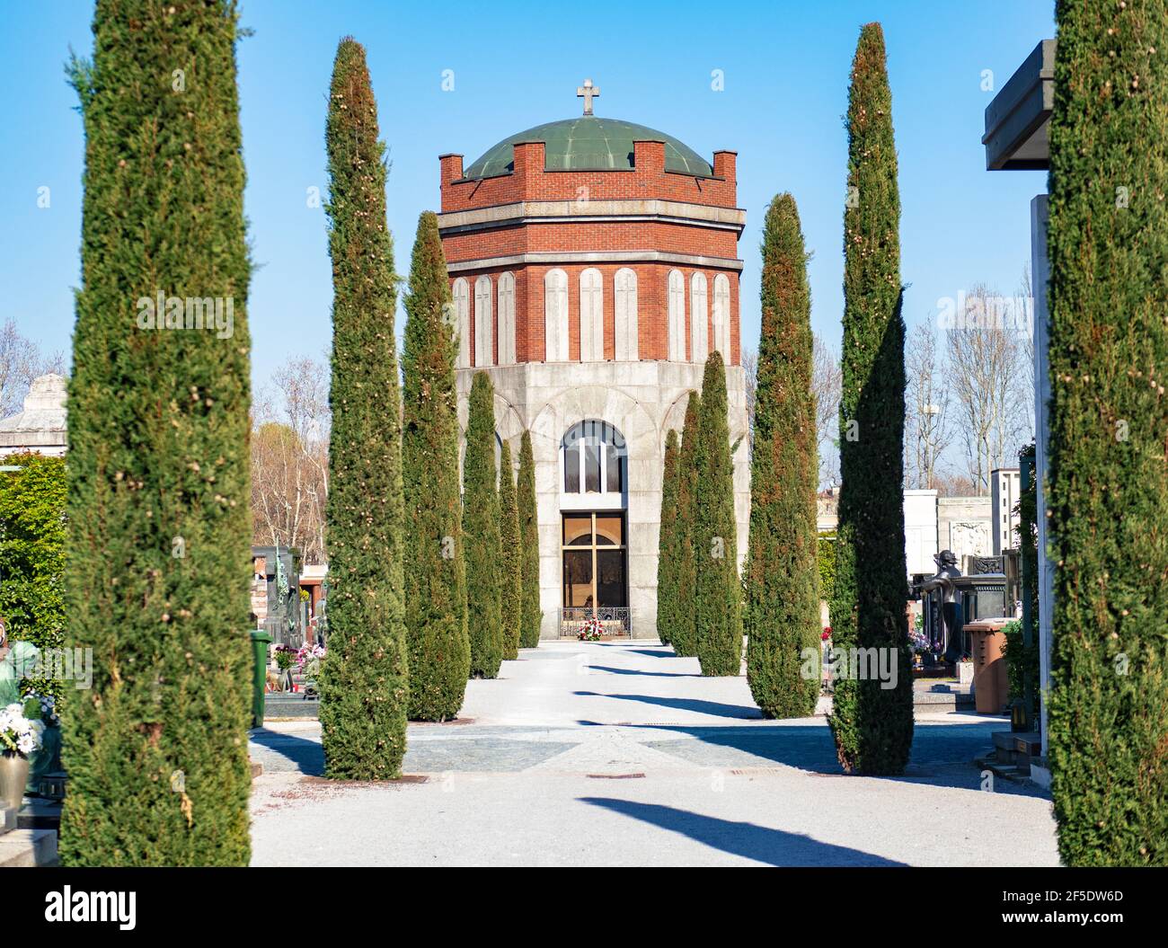 fila di cipressi lungo un viale del cimitero monumentale conduce ad una cappella Foto Stock