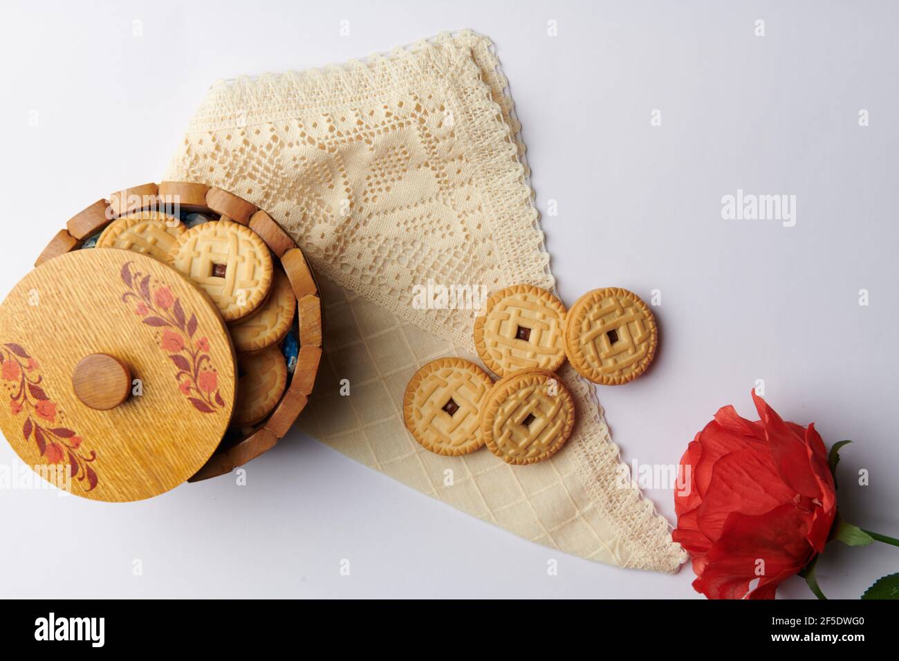 una rosa e biscotti rotondi in una tazza su un tovagliolo su sfondo bianco Foto Stock