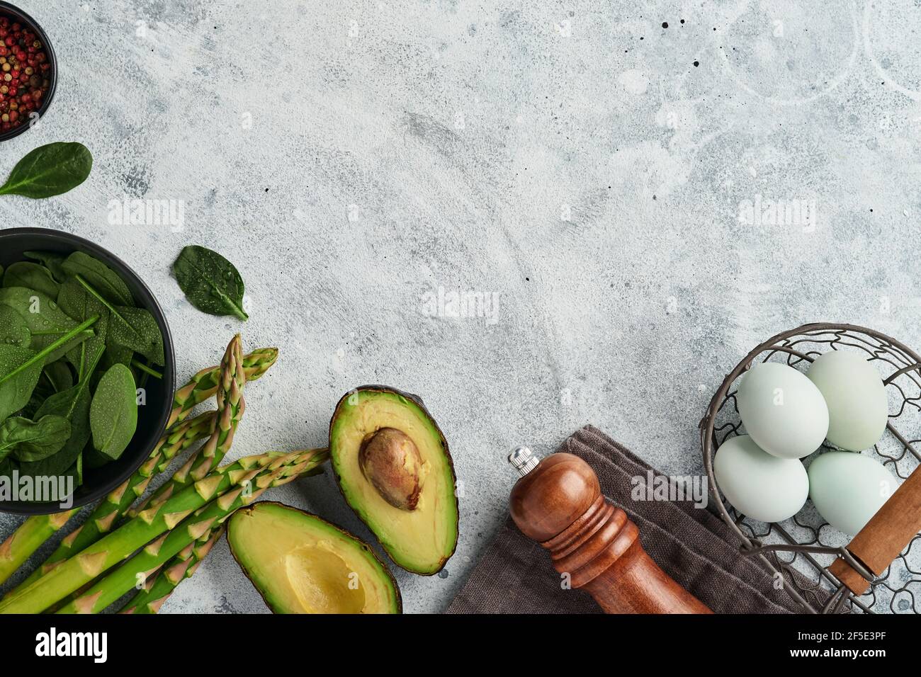 Mazzo di asparagi biologici freschi verdi spinaci, avocado, uova di pollo e pepe condimento su sfondo grigio, vista dall'alto. Cibo cottura sfondo con Foto Stock