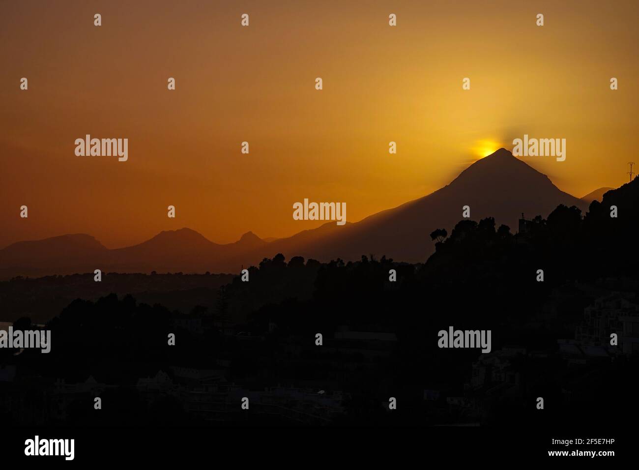 Il sole tramonta dietro la cima triangolare del Puig Campana, vicino a Benidorm, sulla Costa Blanca, in Spagna Foto Stock