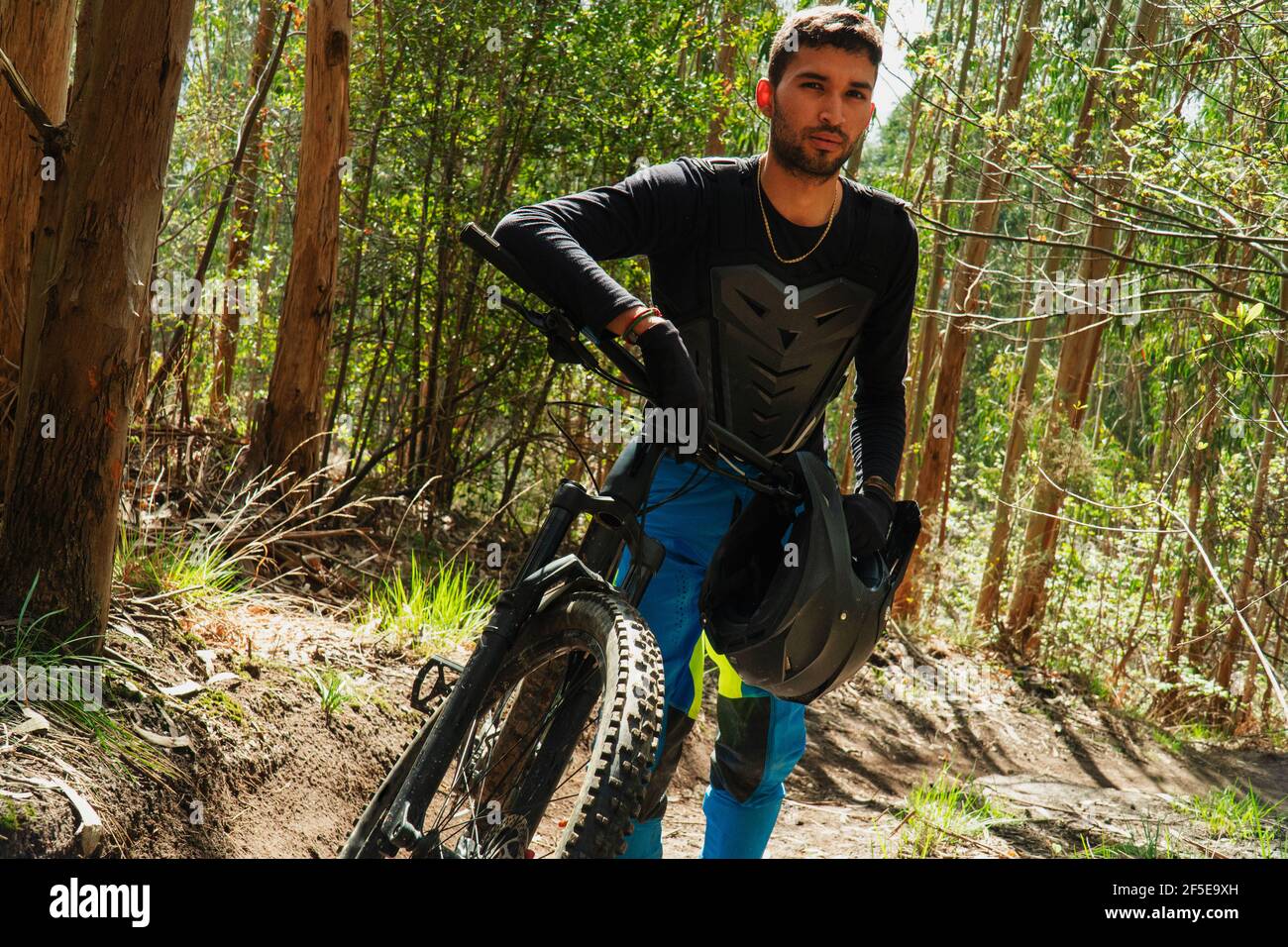 Pedalò teenager latino che cammina lungo il sentiero con la sua montagna pedala attraverso i boschi Foto Stock