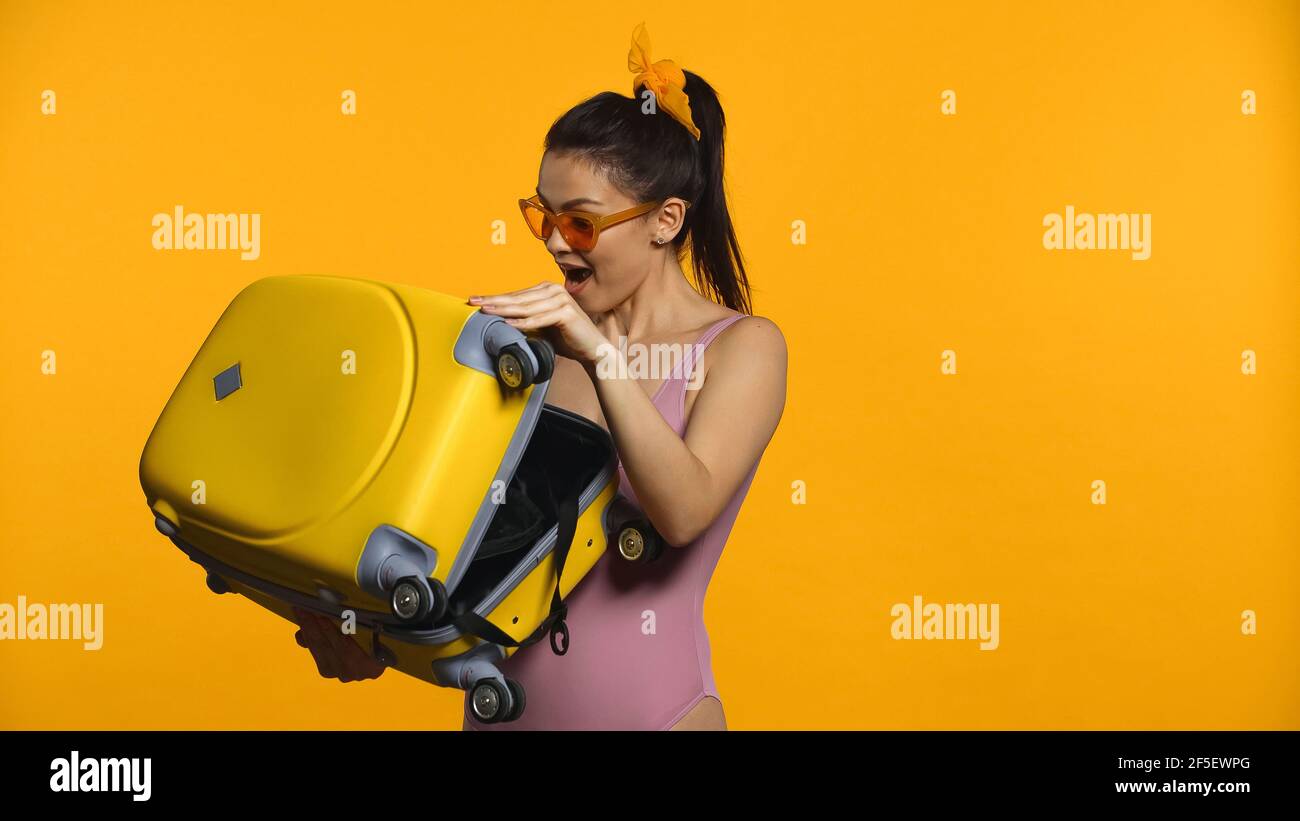 donna eccitata che tiene la valigia isolata sul giallo Foto Stock