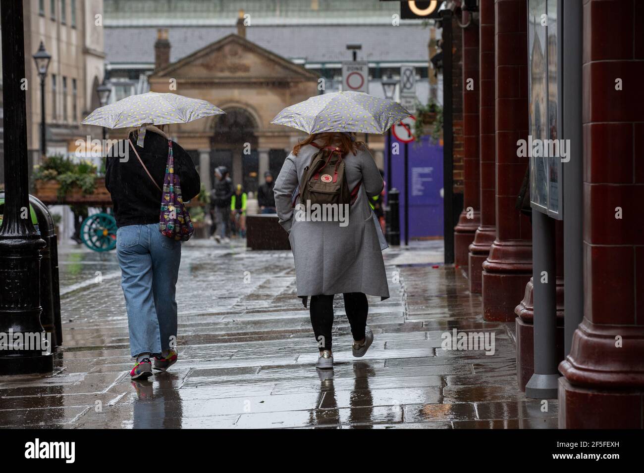 Pedoni che si coprono dalla pioggia tenendo ombrelloni nelle strade deserte del West End di Londra durante le misure di blocco del coronavirus, Inghilterra. Foto Stock