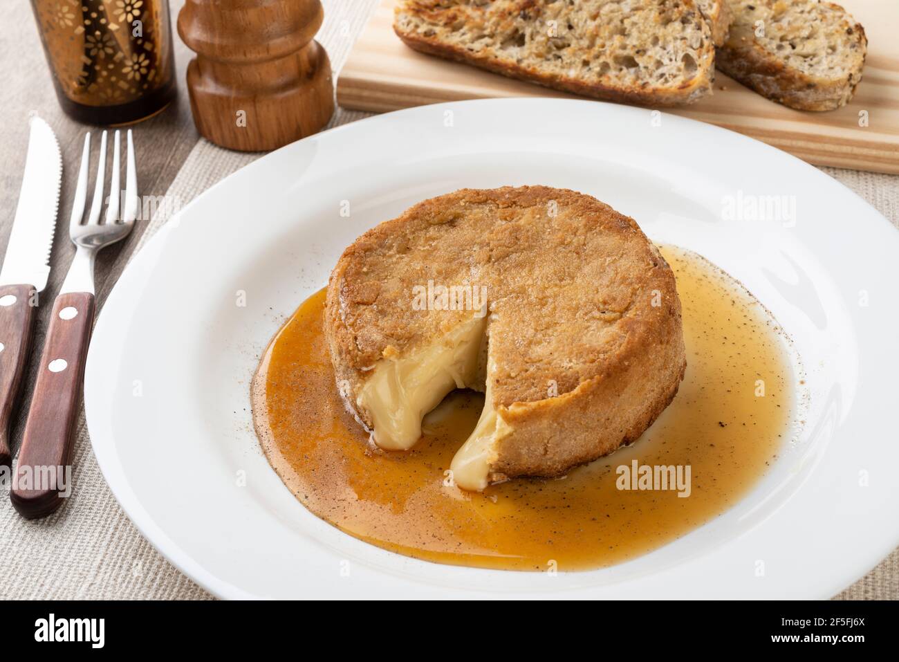 Formaggio camembert impanato con miele, pepe nero e fette di pane grigliate su tavola di legno. Foto Stock