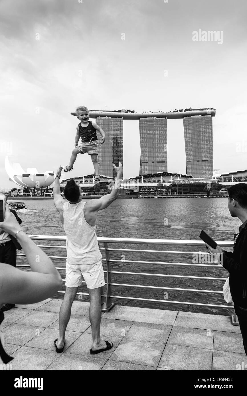 Un Padre getta suo Figlio in aria in posa per una Foto contro lo skyline di Singapore, Singapore, Sud-Est asiatico. Foto Stock