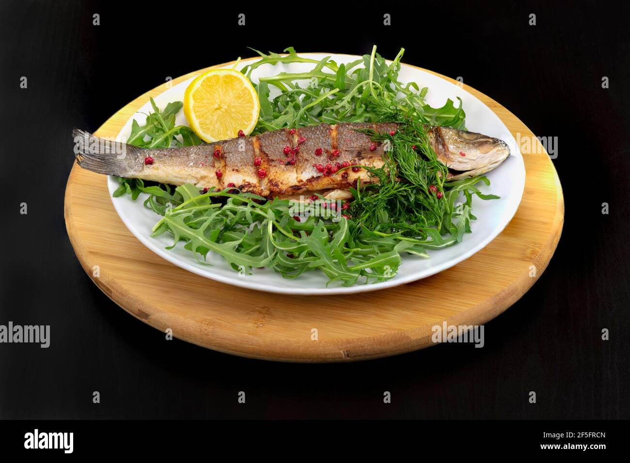 Spigola integrale su un letto di razzo servito con aneto, limone e pepe rosa Foto Stock