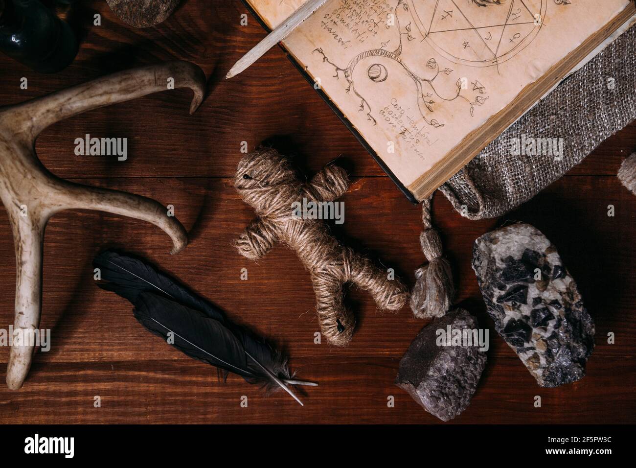 Una bambola voodoo fatta di corda si trova con il vecchio libro Grimoire, circondato da oggetti rituali magici: Candele, pietre, piume di corvo. Concetto di Halloween Foto Stock
