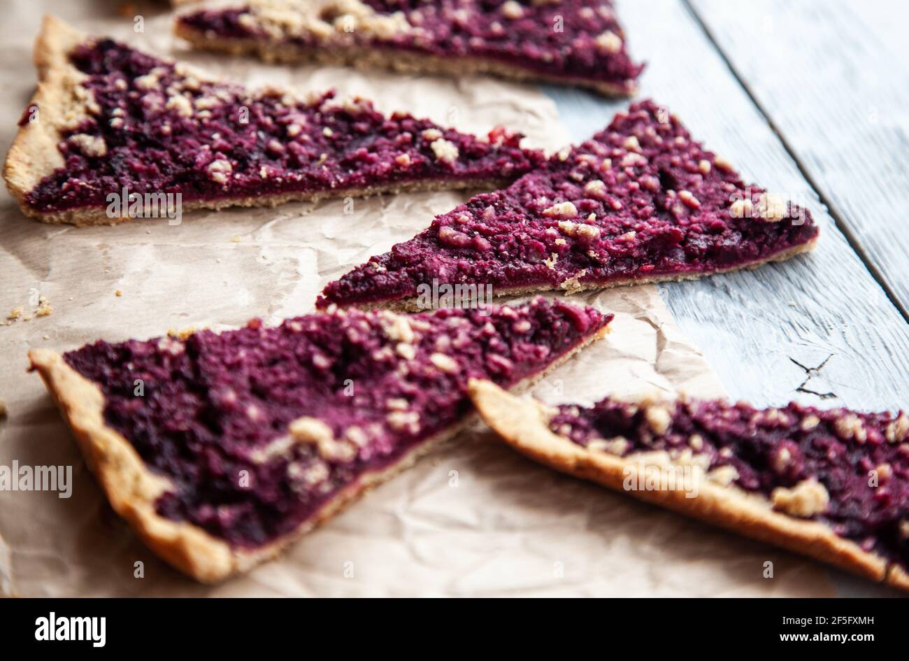 Cinque pezzi di deliziosa crostata di frutti di bosco su pergamena su sfondo grigio di legno. Foto Stock
