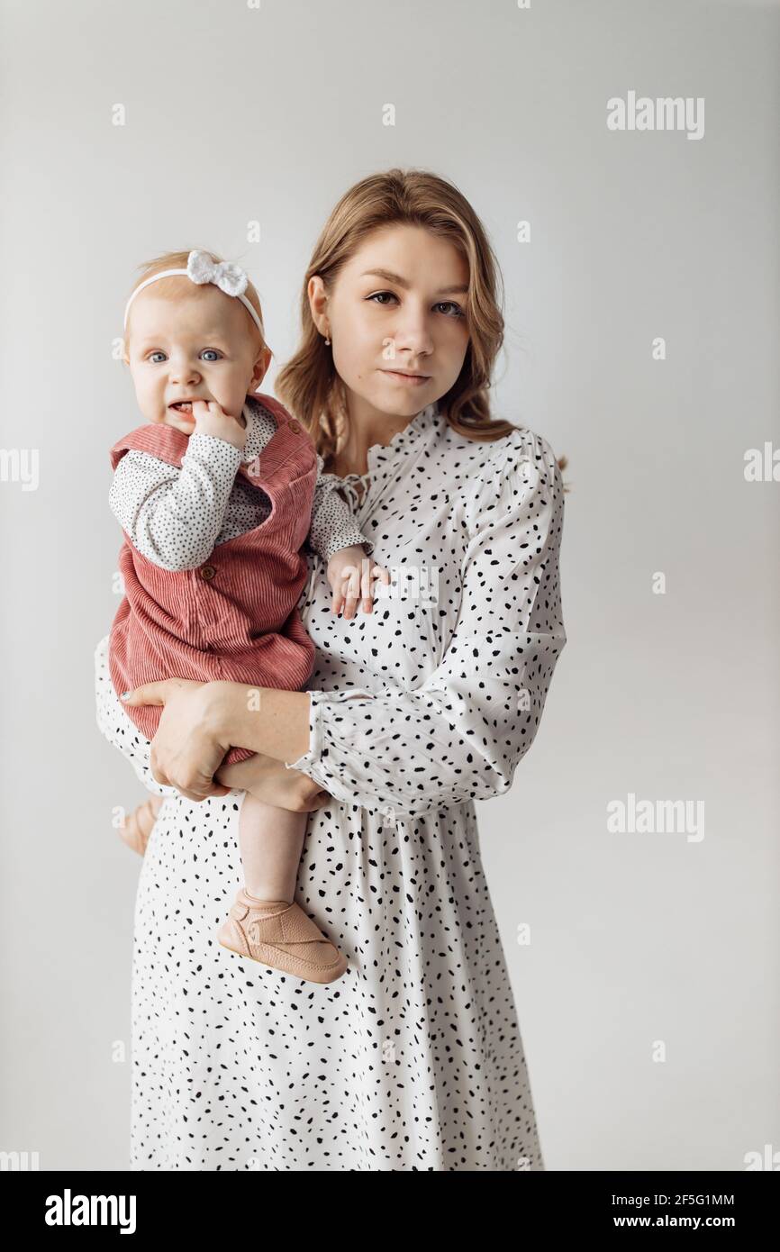 Mamma bionda giovane che tiene una bambina tra le braccia, mamma con la figlia su uno sfondo bianco Foto Stock