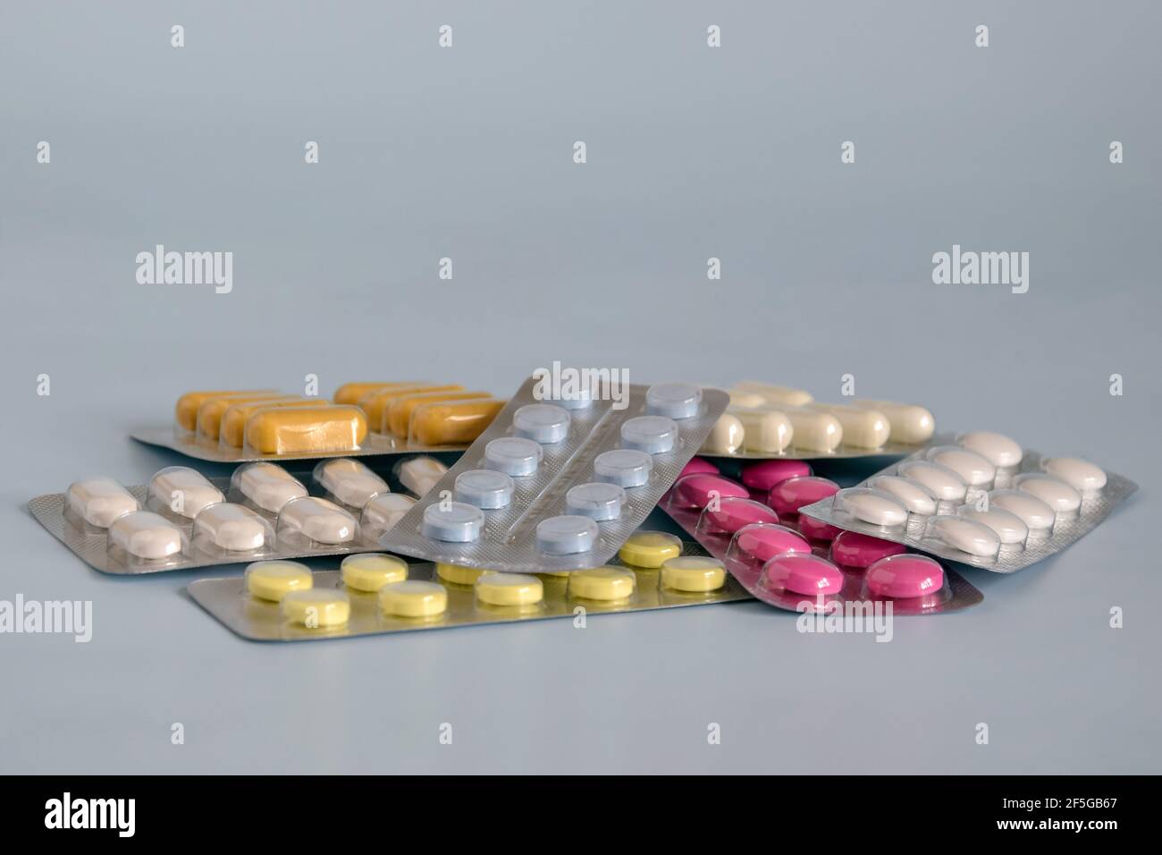 Mucchio di pillole mediche nei colori bianco, blu, marrone, giallo, rosa. Pillole in confezione di plastica su sfondo grigio. Banner panoramico per il design. Primo piano. Foto Stock