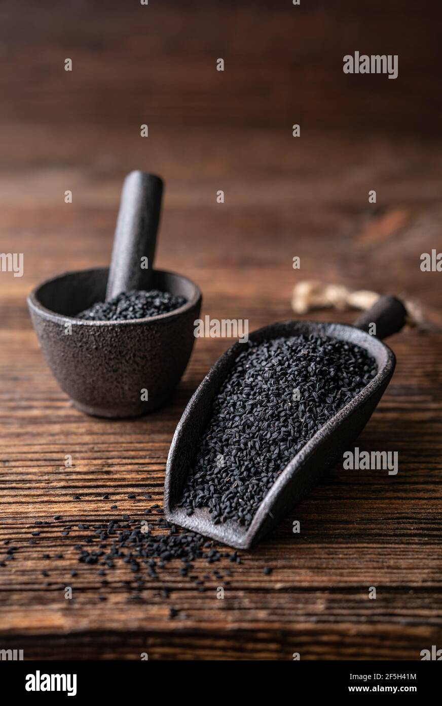 Semi di Nigella sativa conosciuti anche come cumino nero, kalo jeera, kalonji e caraway nero in paletta di ferro e mortaio su fondo rustico di legno Foto Stock