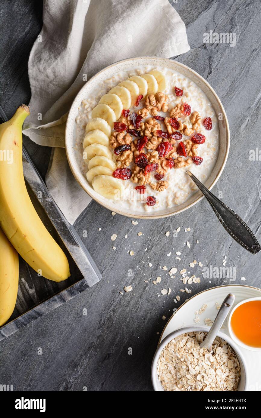 Colazione a base di cereali sani, farinata d'avena con fette di banana, mirtilli rossi secchi, noce, servita con miele in una ciotola Foto Stock