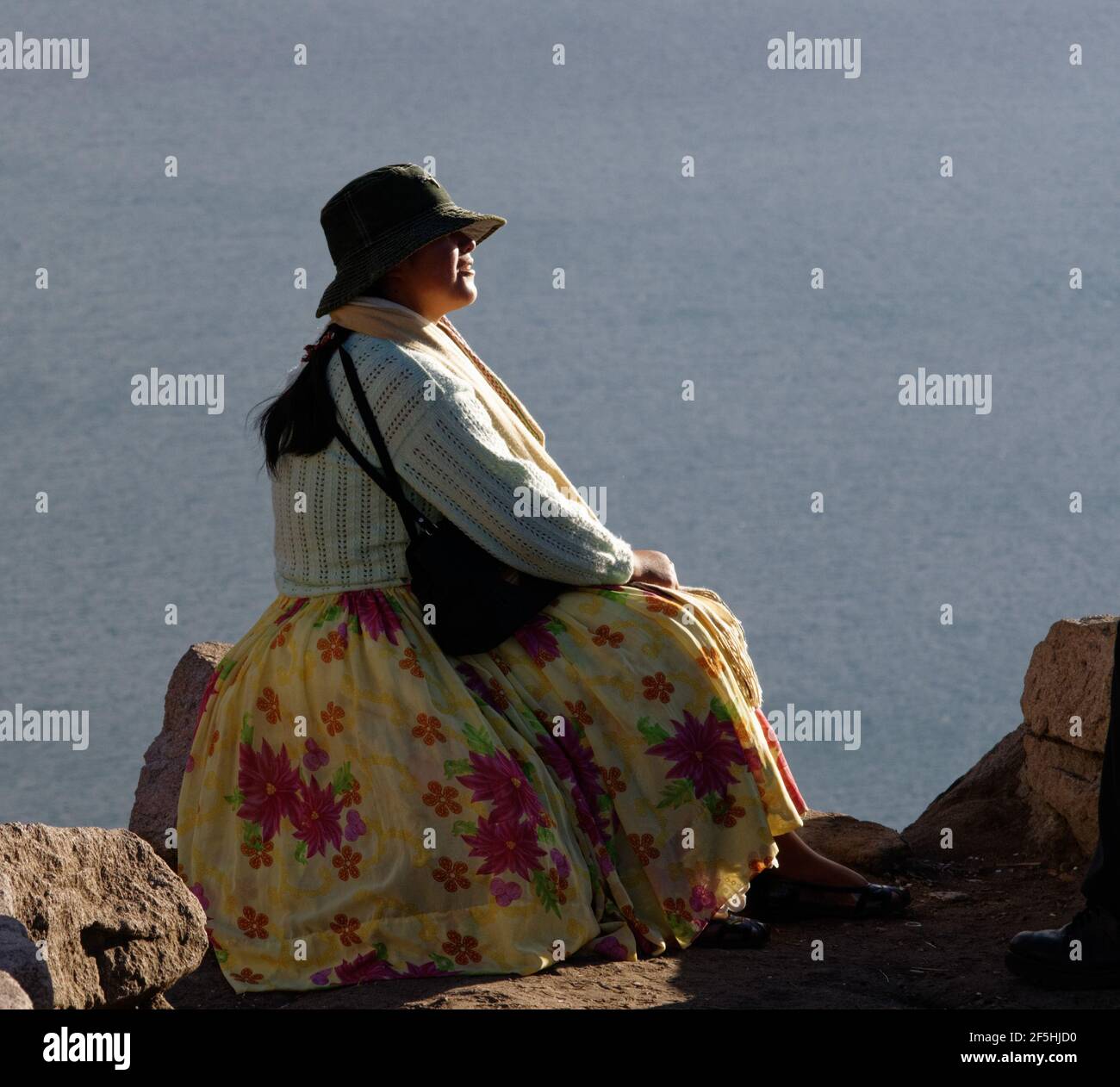 Una donna boliviana in abito tradizionale seduta con lago Titicaca sullo sfondo Foto Stock