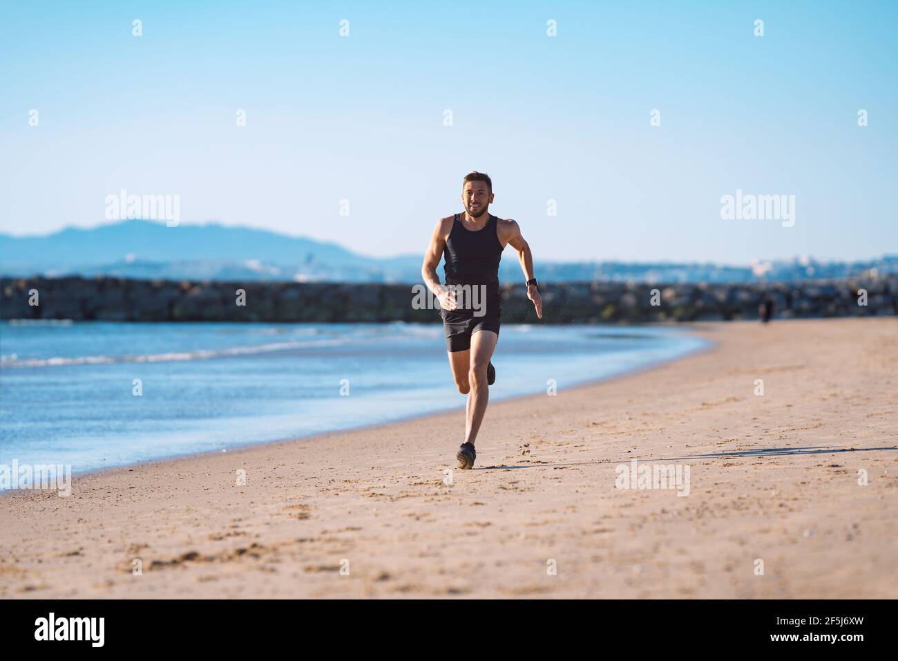 Corridore in movimento. Giovane atletico sportivo che corre lungo la spiaggia Foto Stock