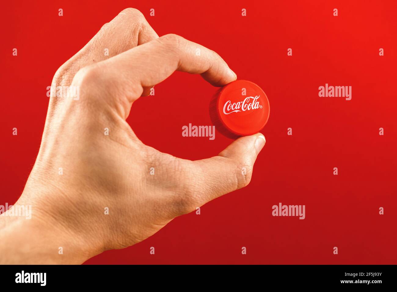 Kharkov, Ucraina - 24 marzo 2021: Coca cola cappuccio con logo in mano uomo, su un backcground rosso Foto Stock